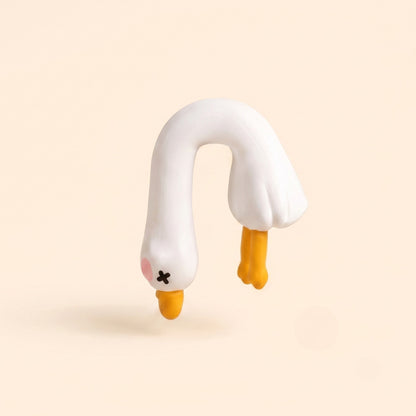 A studio product shot of the By1994 mini duck figurine in the Dangling pose, featuring an upside-down hanging white resin duck with X-eyes and yellow feet on a cream backdrop.