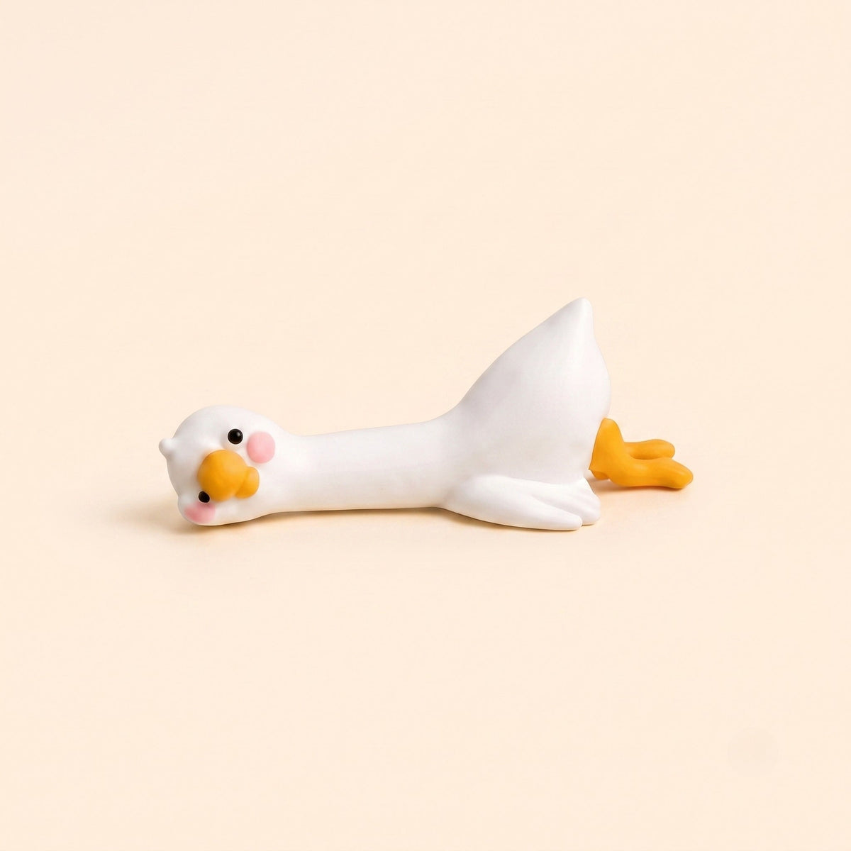 A minimalist studio product shot of the By1994 mini duck figurine in the Lying pose, showing a cute white resin duck resting flat on its belly against a light cream backdrop.