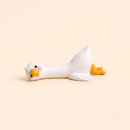A minimalist studio product shot of the By1994 mini duck figurine in the Lying pose, showing a cute white resin duck resting flat on its belly against a light cream backdrop.